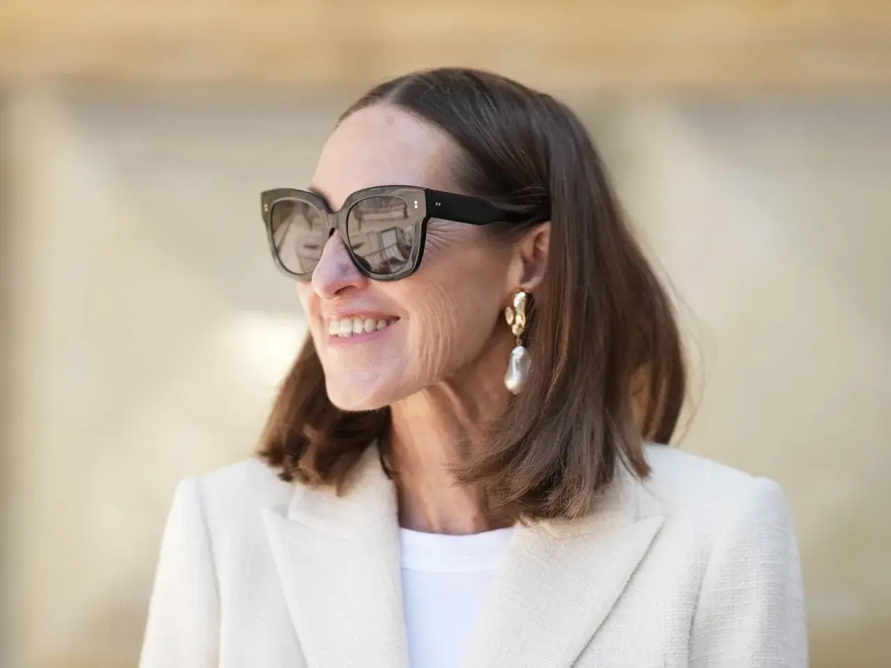 Stilvolle Frau mit mittellangem Haar, Sonnenbrille und auffälligem Ohrring. Perfekt für unkomplizierte Frisuren mittellang ab 50.