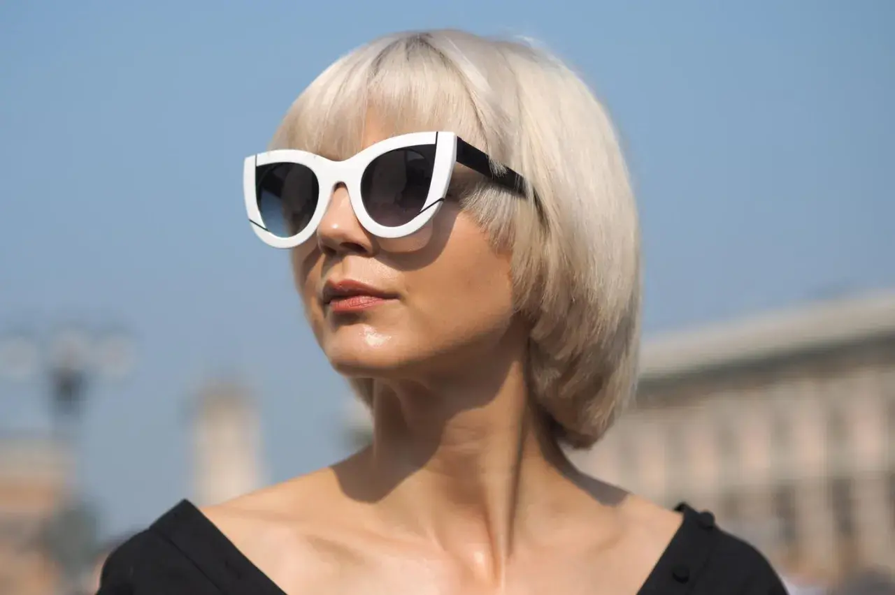 Blonde Frau mit Pagenschnitt und auffälliger Sonnenbrille blickt nach rechts.