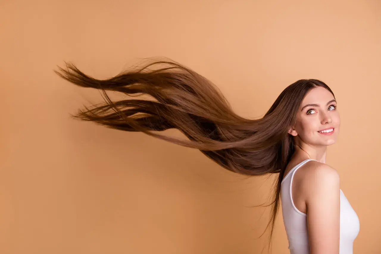 Frau mit langen, braunen Haaren, die im Wind wehen. Sie lächelt und blickt zur Seite.