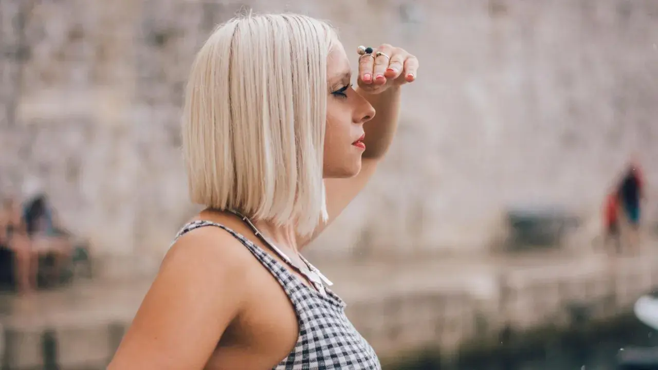 Frau mit **long bob blond** schaut in die Ferne, die Hand schützend über die Augen gelegt.