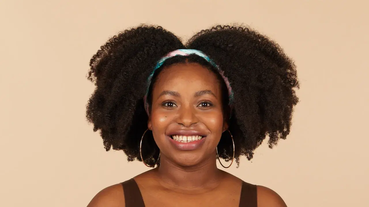 Lächelnde Frau mit voluminösen 4c Locken und einem bunten Haarband.
