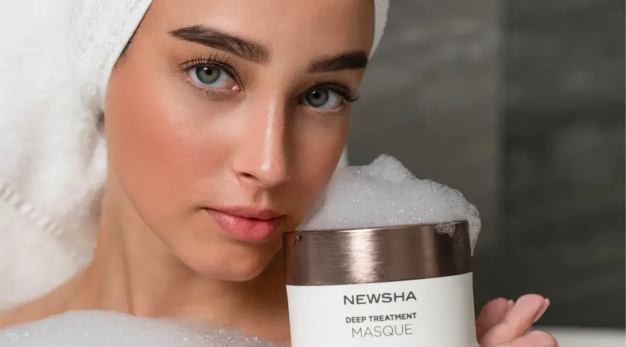 Frau mit Handtuch auf dem Kopf hält eine NEWSHA Haarmaske mit Schaum. Die Anwendung der Haarmaske verspricht Pflege.