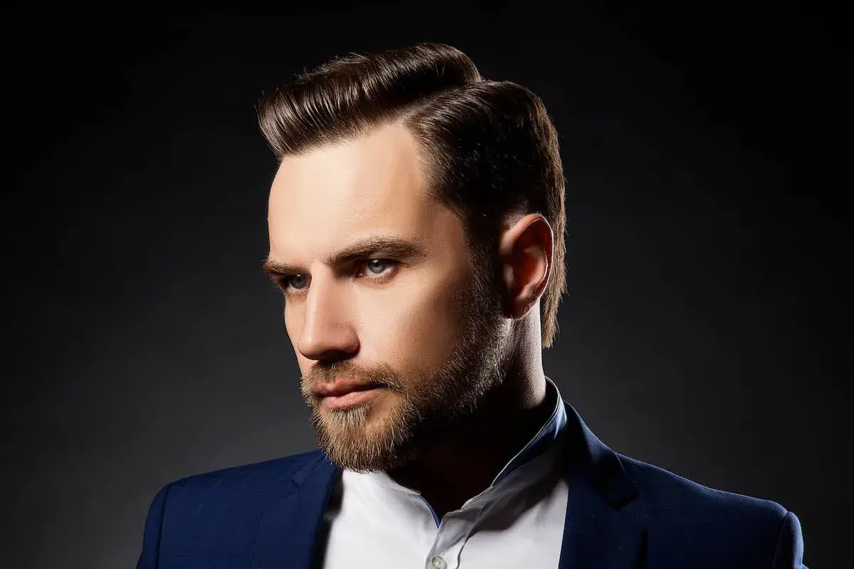 Ein Mann mit Bart und einem eleganten Seitenscheitel, gekleidet in einem blauen Anzug.