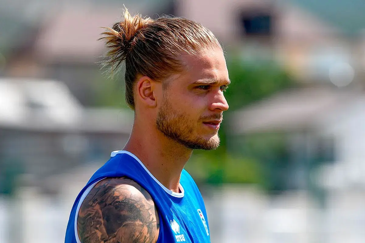 Ein Mann mit einem lässigen **man bun ohne bart**, trägt ein blaues Trikot. Sein Blick ist nach rechts gerichtet.