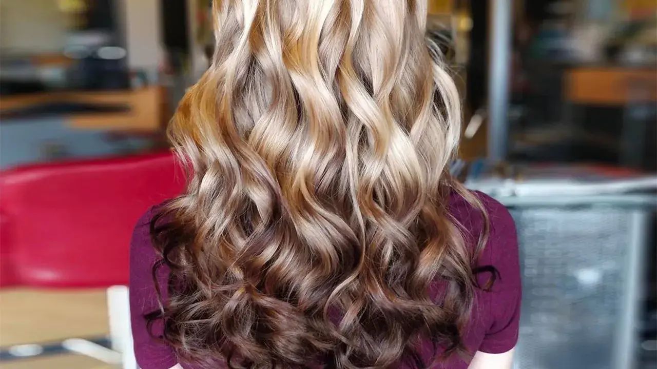 Langes, welliges Haar mit einem **Reverse Balayage**-Effekt, der von hellblond zu dunkleren Brauntönen übergeht.