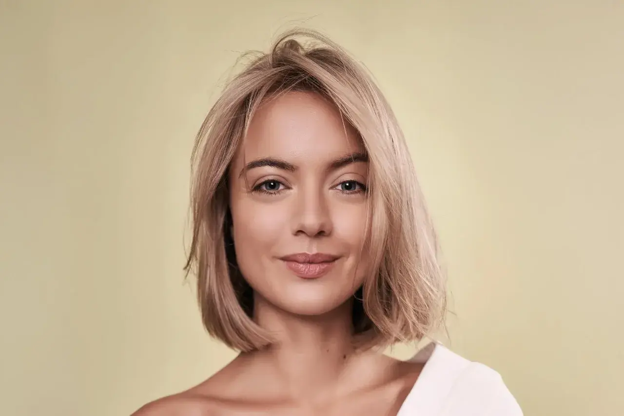 Porträt einer Frau mit blondem Haar und einem sanften Lächeln. Ihr Haar ist kurz geschnitten, wie ein **calligraphy cut**, und fällt locker um ihr Gesicht.