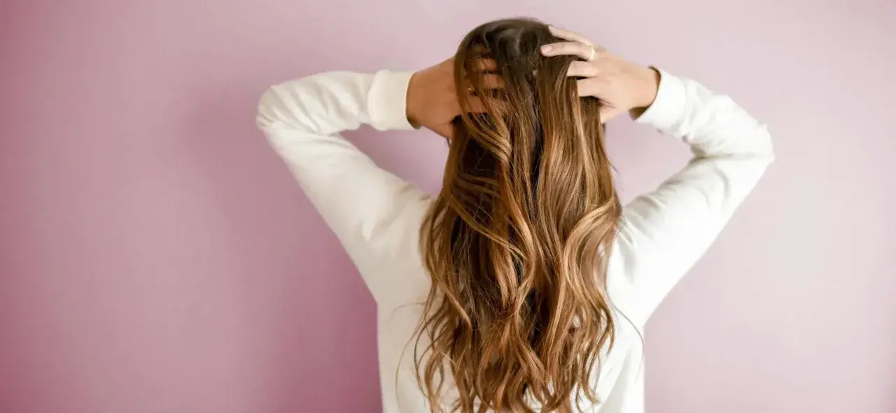 Frau mit langen, welligen 2a Haaren, die sie mit den Händen im Nacken hält.