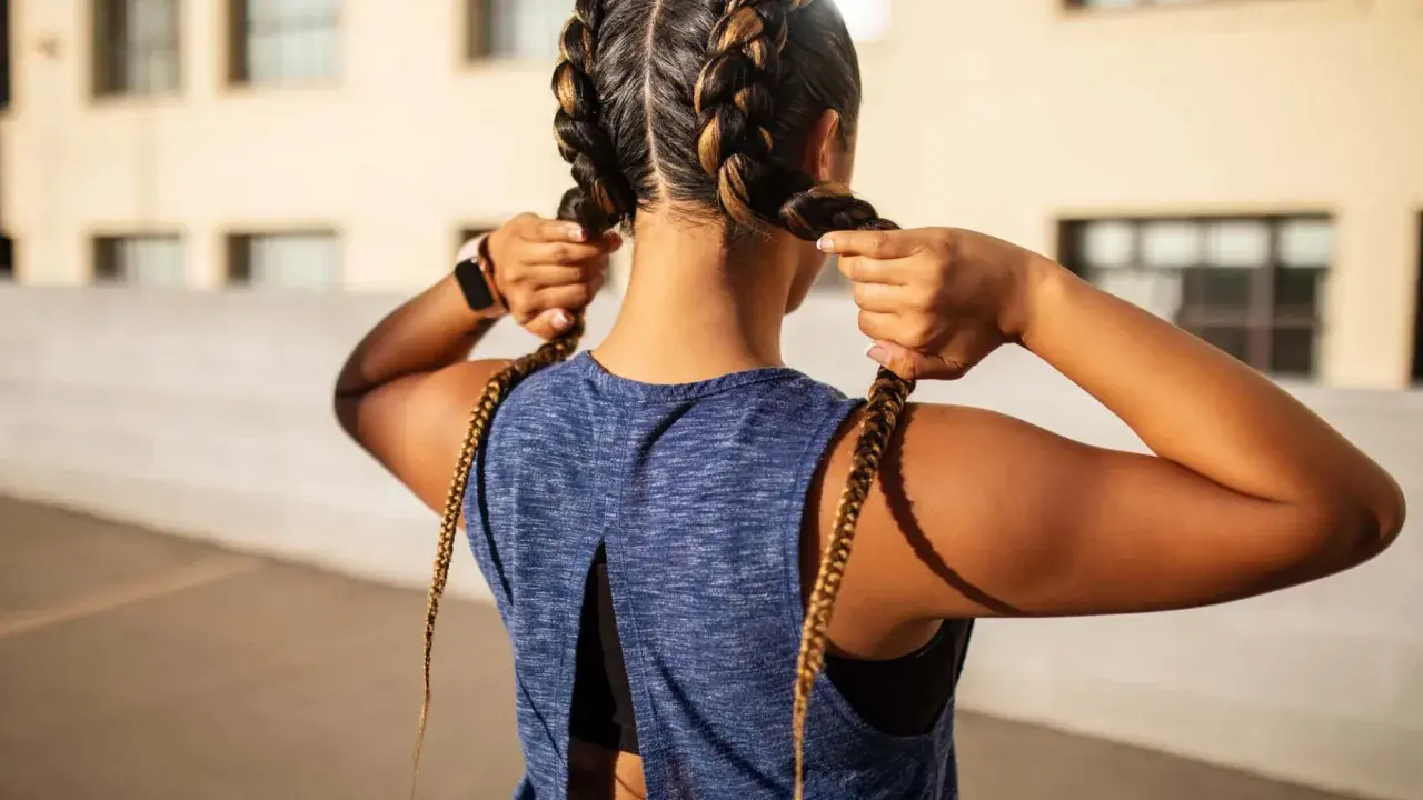 Sportliche Frau mit boxer braids, die ihre Zöpfe zurechtrückt.