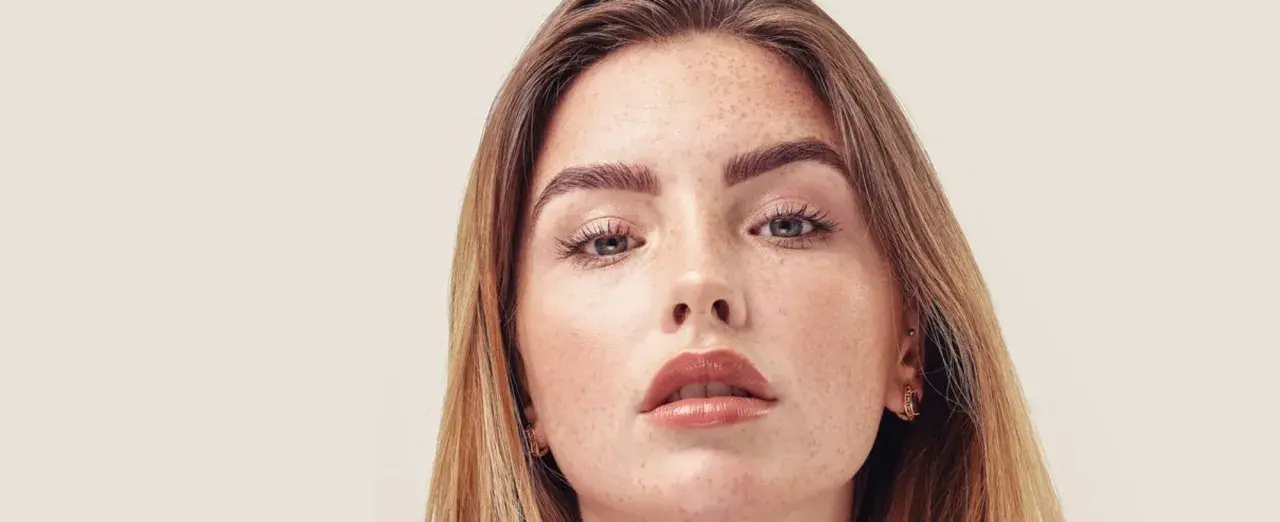 Nahaufnahme einer jungen Frau mit Sommersprossen und dunkelblond hellbraunen Haaren, die sanft über ihre Schultern fallen.