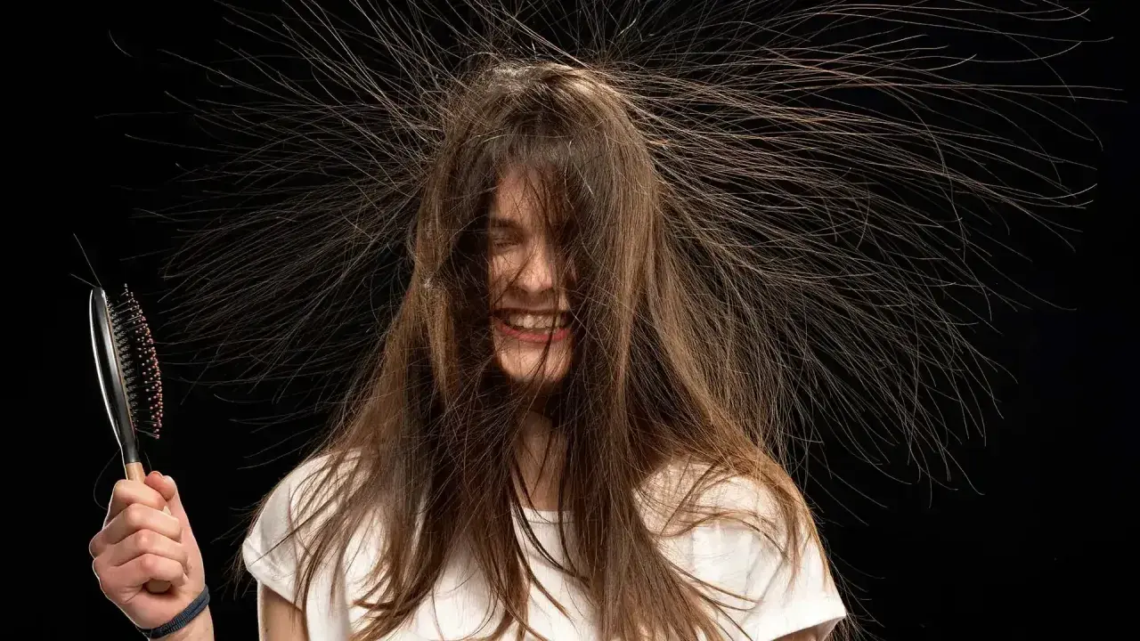 Lachende Frau mit Haaren, die elektrisch abstehen. Eine Bürste in der Hand verstärkt den Eindruck von statischer Aufladung.