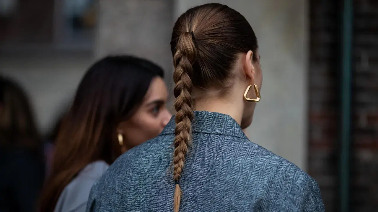 Eine Frau mit geflochtenen Haaren trägt einen grauen Blazer und auffällige goldene Ohrringe.