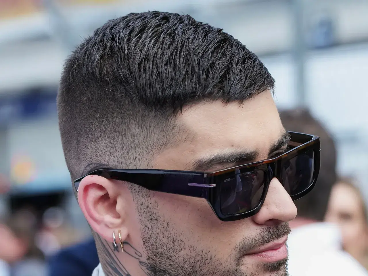 Mann mit stylischem herren kurzhaarschnitt, Sonnenbrille und Ohrringen.