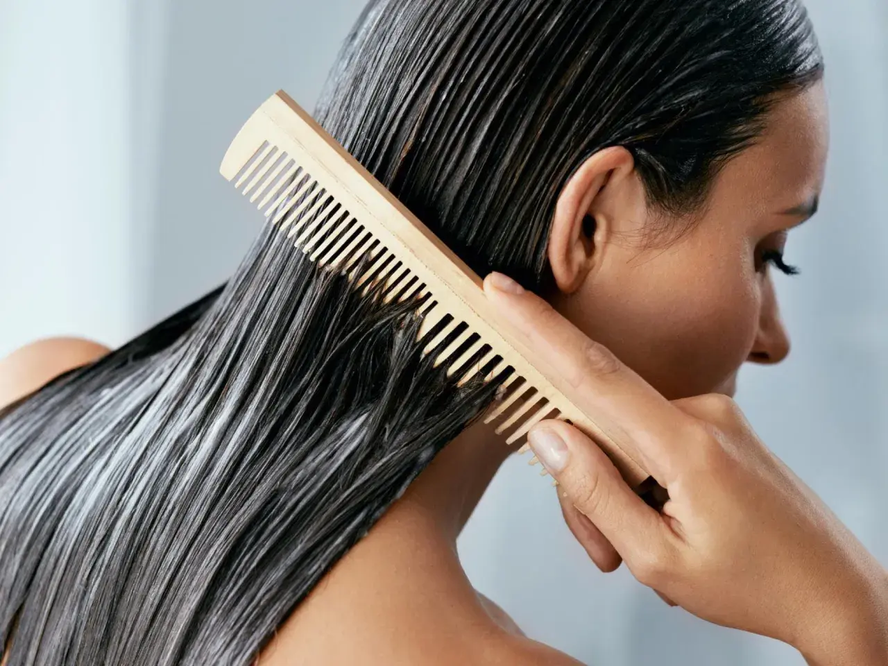 Frau kämmt nasses Haar mit Conditioner. Was ist Conditioner? Es macht das Haar weich und glänzend.