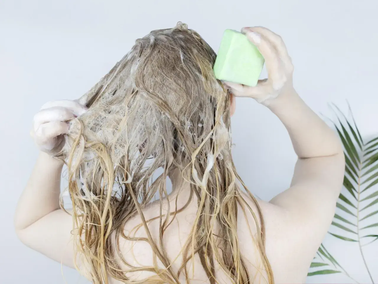 Frau wäscht sich die Haare mit einem festen Shampoo-Riegel. Die Herstellung von Shampoo kann so einfach sein.