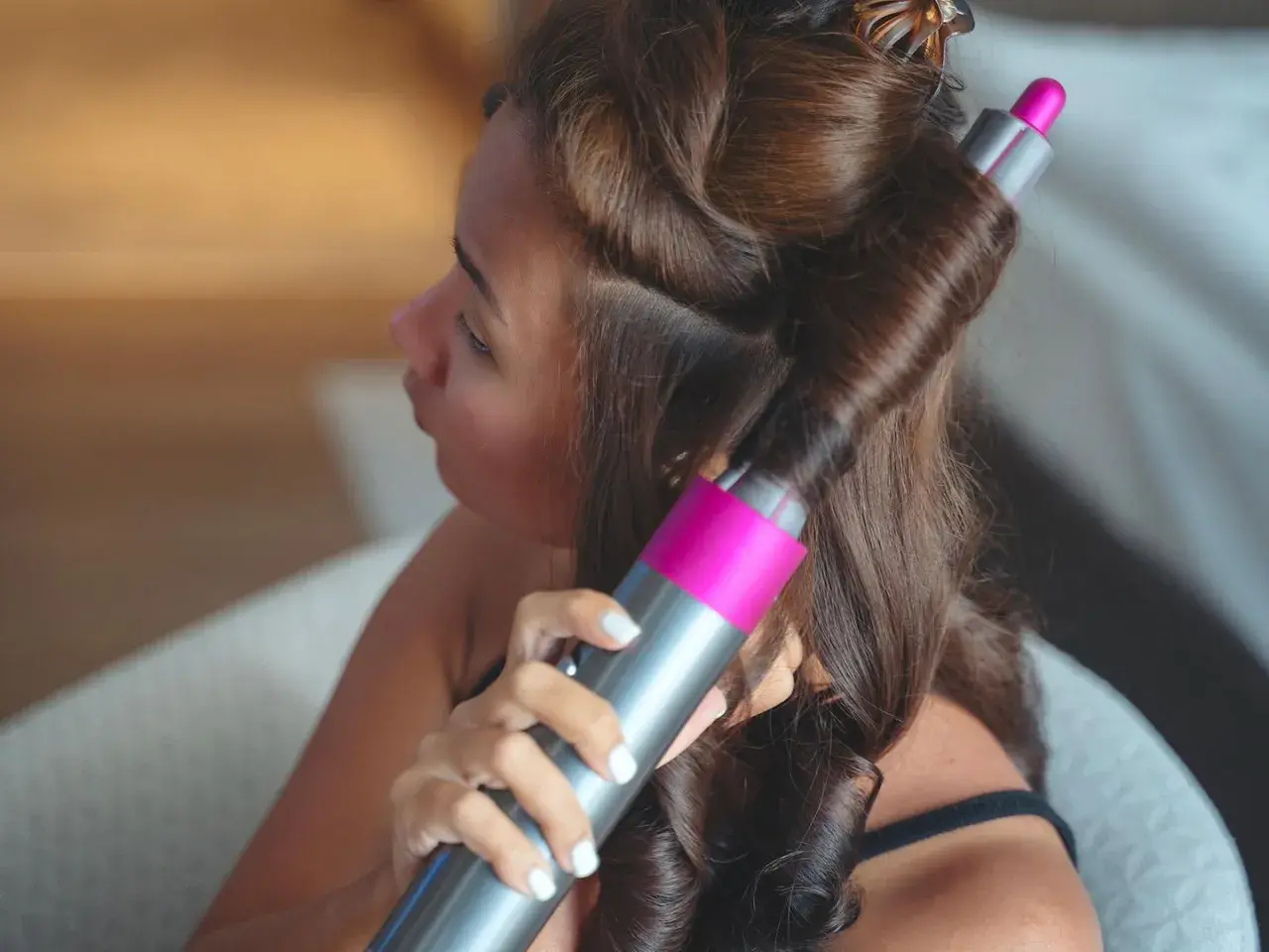 Frau stylt ihre Haare mit einem Lockenstab, um schöne Locken zu kreieren.