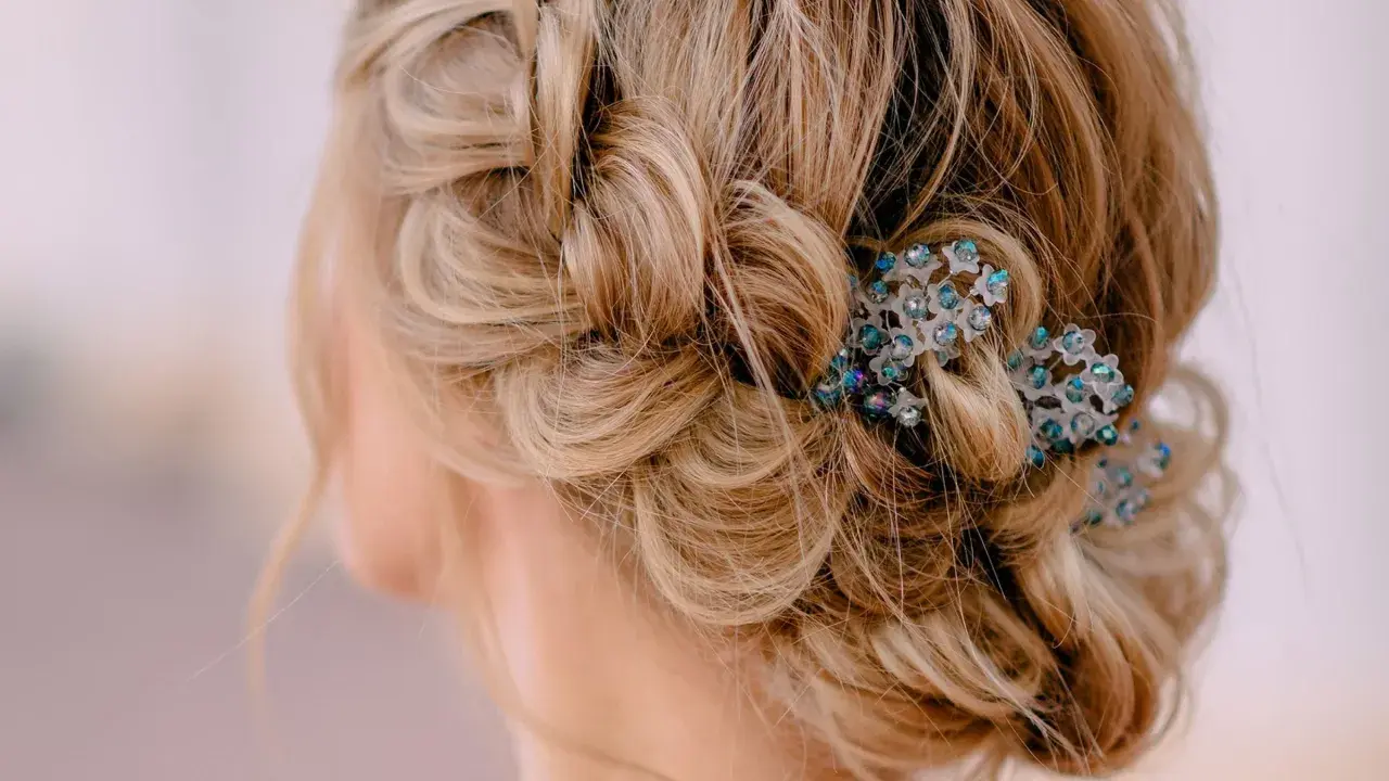 Zarte, geflochtene Strähnen und lockere Wellen ergeben eine elegante Hochsteckfrisur, verziert mit funkelnden Haarschmuck. Einfach und doch raffiniert.