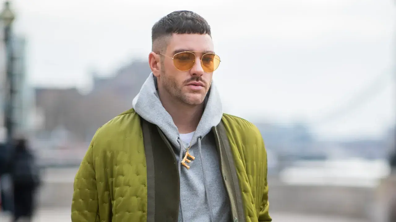 Mann mit French Crop High Fade, gelben Sonnenbrillen und Bomberjacke.