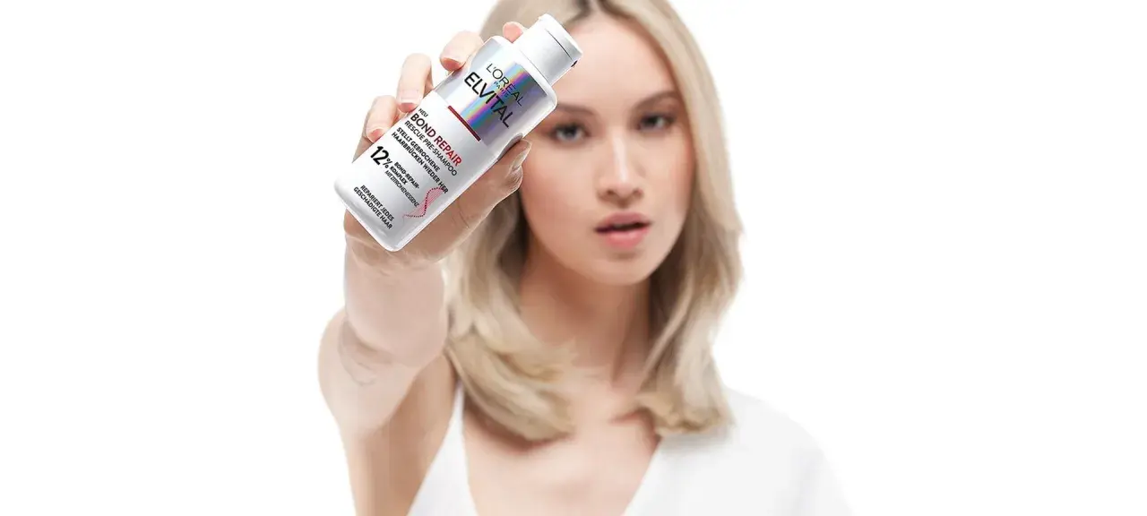 Frau hält L'Oréal Elvital Bond Repair Pre-Shampoo, um trockene Haare zu retten.