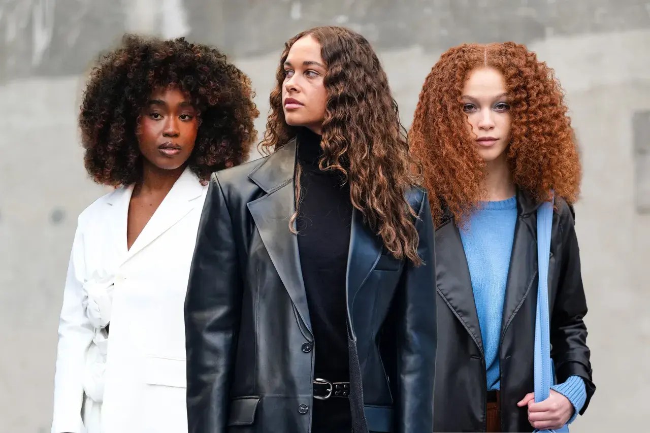 Drei Frauen mit voluminösen Locken, die sich fragen, wie oft locken waschen. Eine trägt Weiß, die andere Schwarz und die dritte Blau.