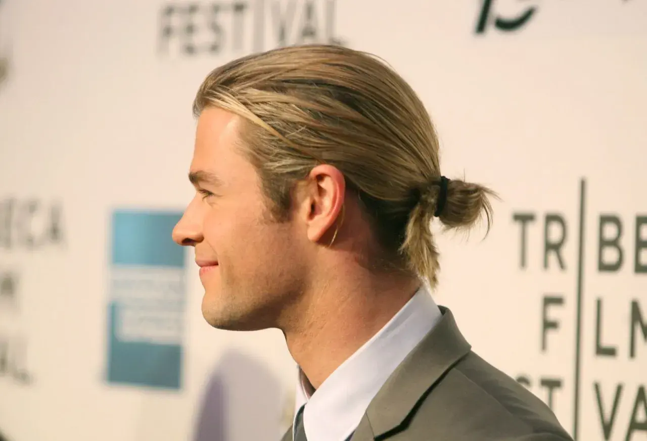 Jungs Frisur lang Surfer-Look: Blondes Haar zu einem kleinen Dutt gebunden, lässig und cool.