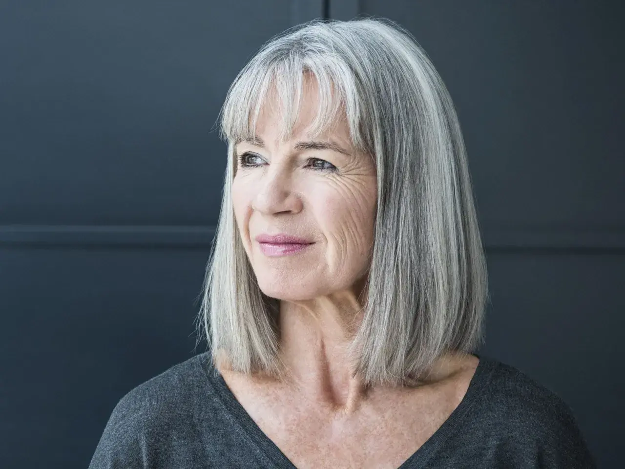 Porträt einer Frau mit stilvollen grauen Haaren, die nachdenklich zur Seite blickt.