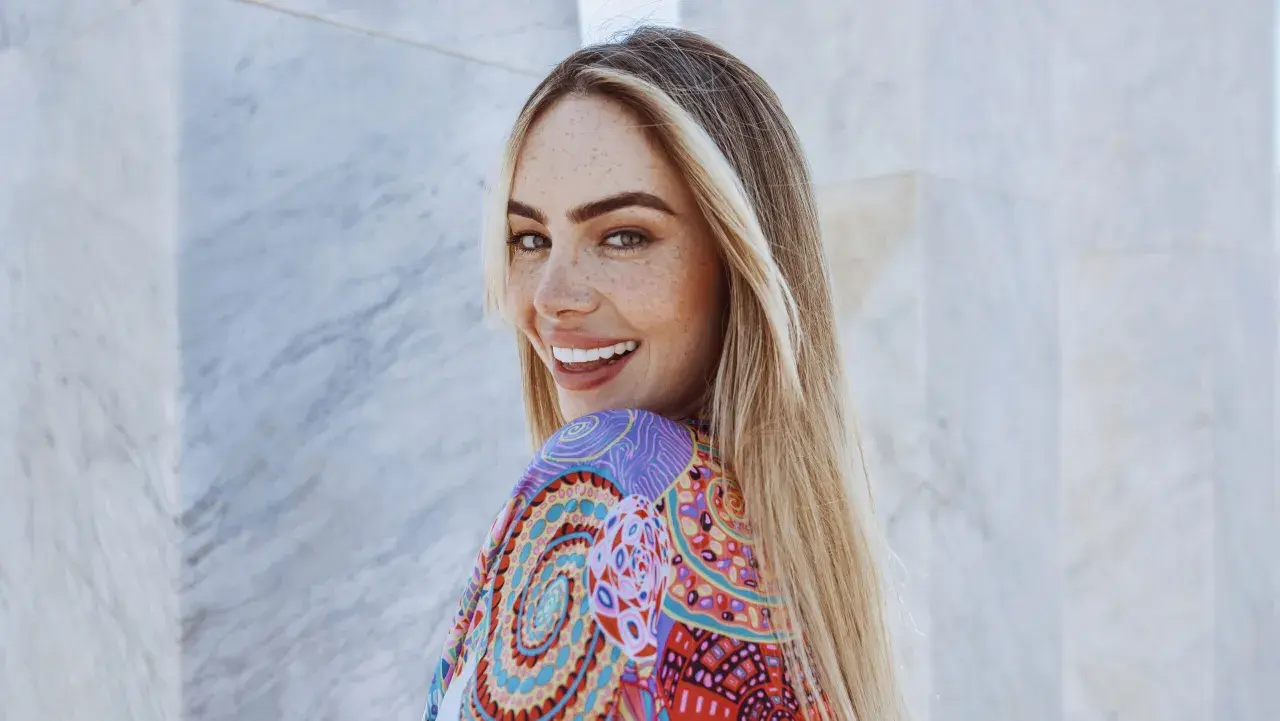 Frau mit Sommersprossen und einer **scandinavian hairline** lächelt in die Kamera, trägt ein buntes Kleid.