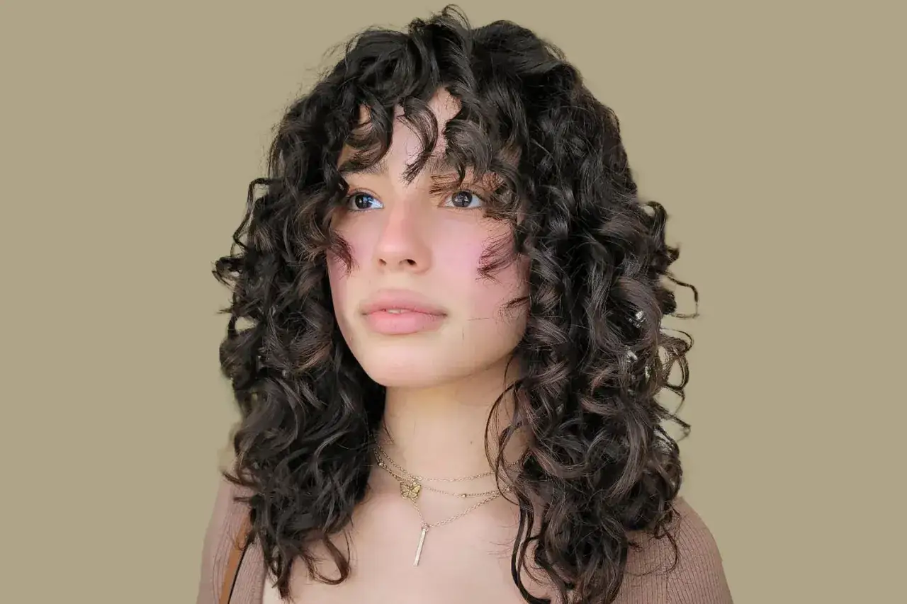 Ein junges Mädchen mit einem vollen pony mit locken, das nachdenklich zur Seite blickt. Ihr dunkles, lockiges Haar umrahmt ihr Gesicht.