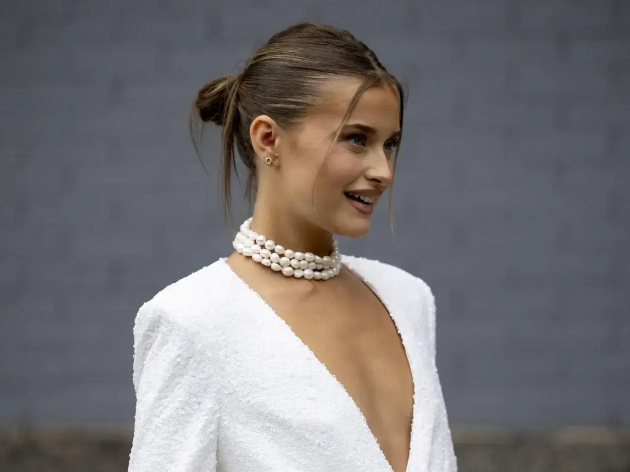 Elegante Frau mit Dutt und Perlenkette, bereit für Silvester-Frisuren.