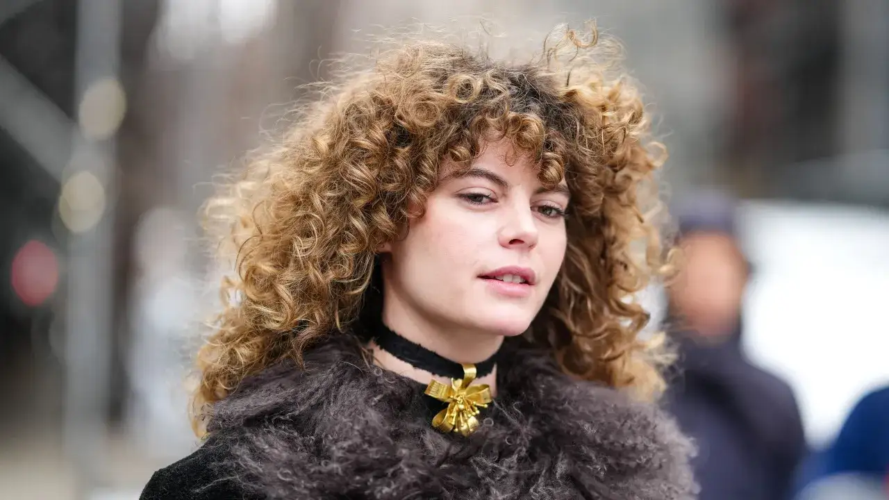 Frau mit voluminösem, naturkrausem Haar und einem goldenen Anhänger an einem schwarzen Choker.