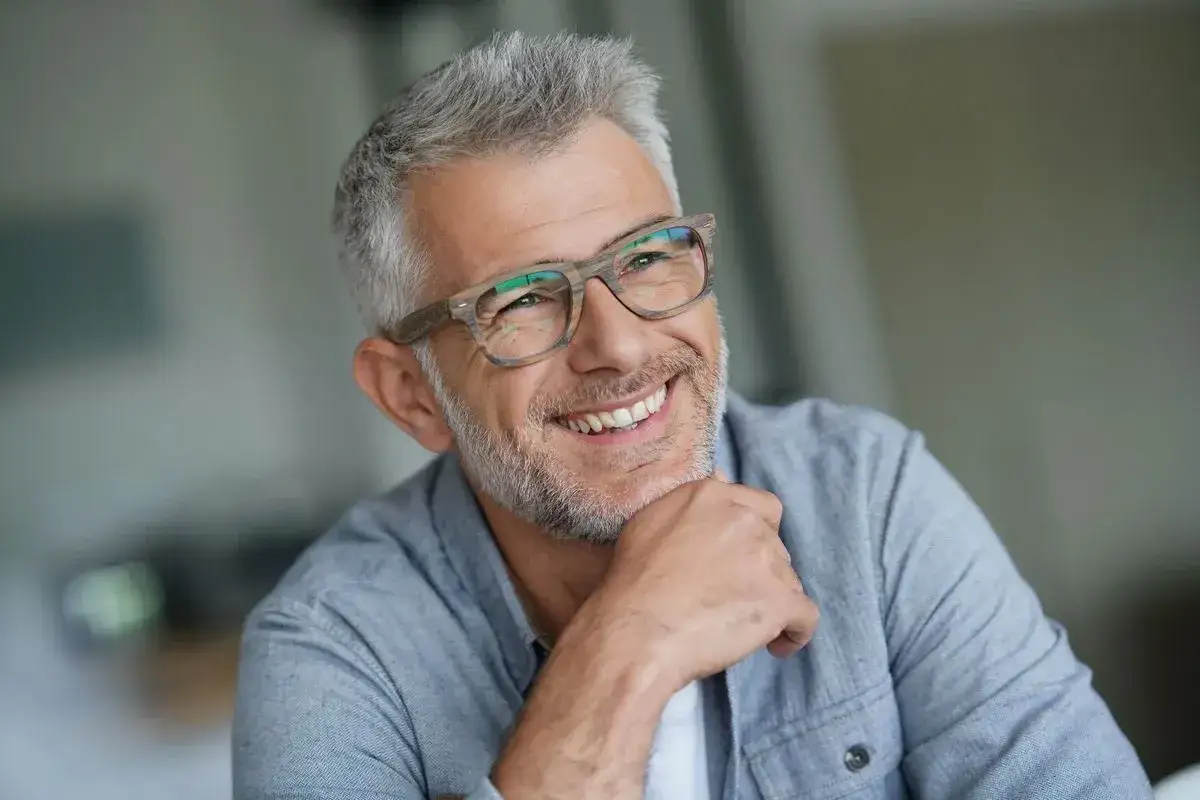 Lächelnder Mann mit Brille und grauem Haar, ein Beispiel für stilvolle herren frisuren ab 50.