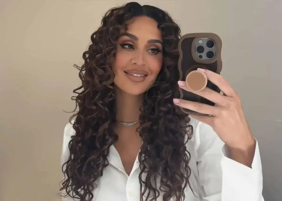 Frau mit vollen, definierten Locken und einem Handy in der Hand.
