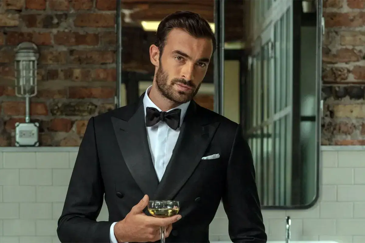 Ein Mann mit gepflegten Haaren nach hinten, im Smoking, hält ein Glas Champagner.