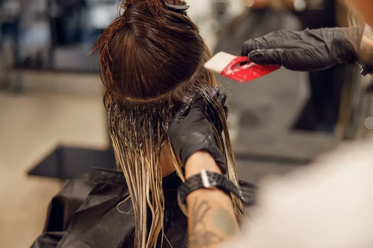 Friseur trägt Handschuhe und trägt Farbe auf das Haar auf. Eine Coloration verändert die Haarfarbe.