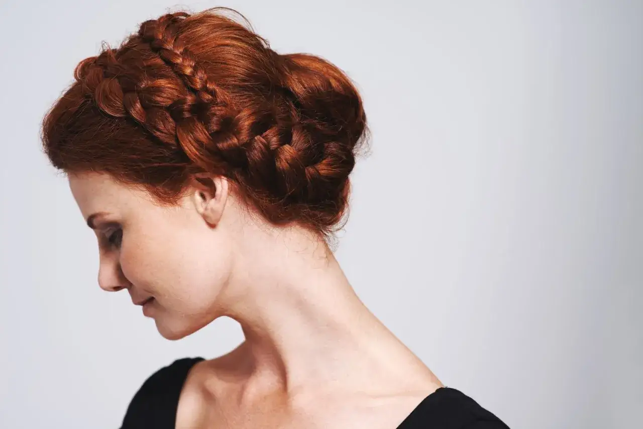 Eine Frau mit roten Haaren trägt mittellange Hochsteckfrisuren, die zu einem kunstvollen Dutt geflochten sind.