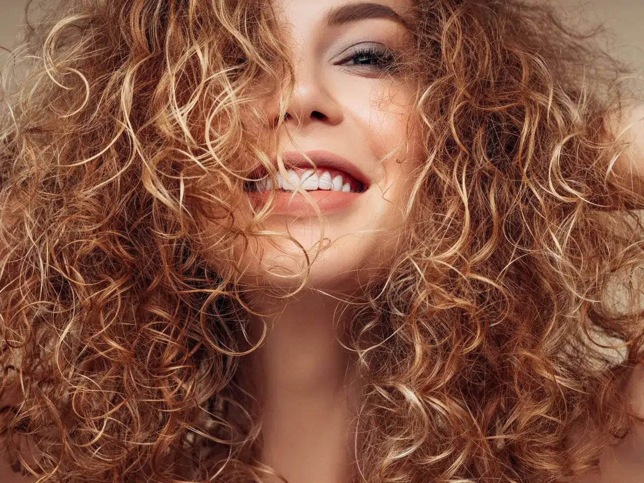 Strahlendes Lächeln einer Frau mit voluminöser Dauerwelle. Ihre Locken umrahmen ihr Gesicht und betonen ihre natürliche Schönheit.