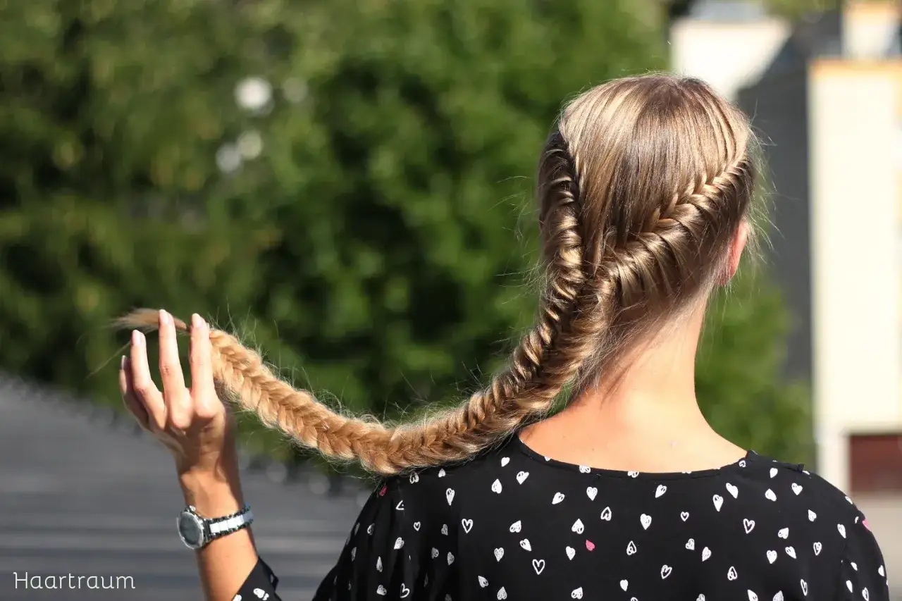 Ein Fischgr&auml;tenzopf, der zeigt, wie haare zu lang werden k&ouml;nnen. Die Hand h&auml;lt die Spitze des geflochtenen Zopfes.