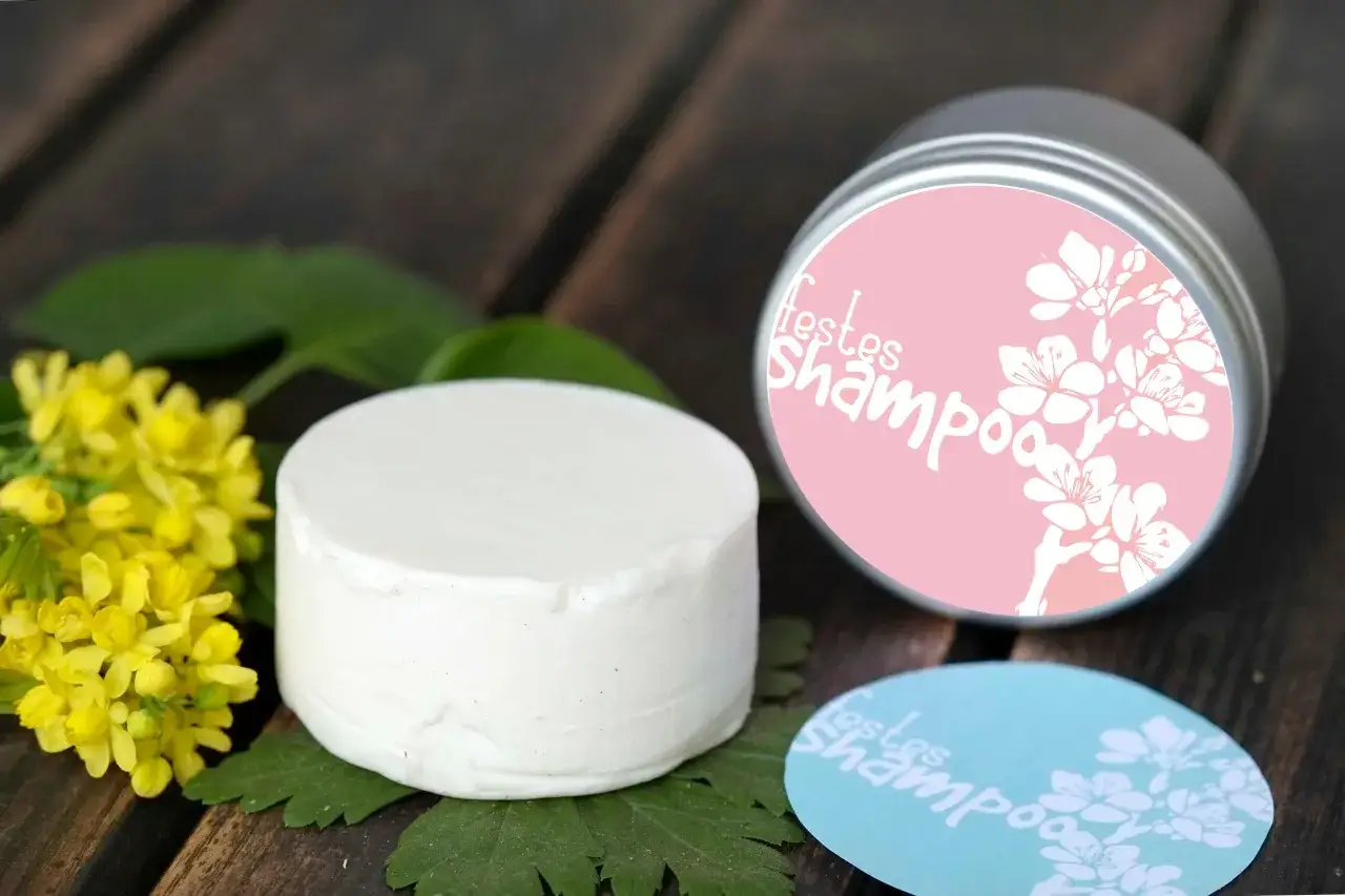 Ein weißer fester Shampoo-Block neben gelben Blüten. Eine Dose mit dem Aufdruck
