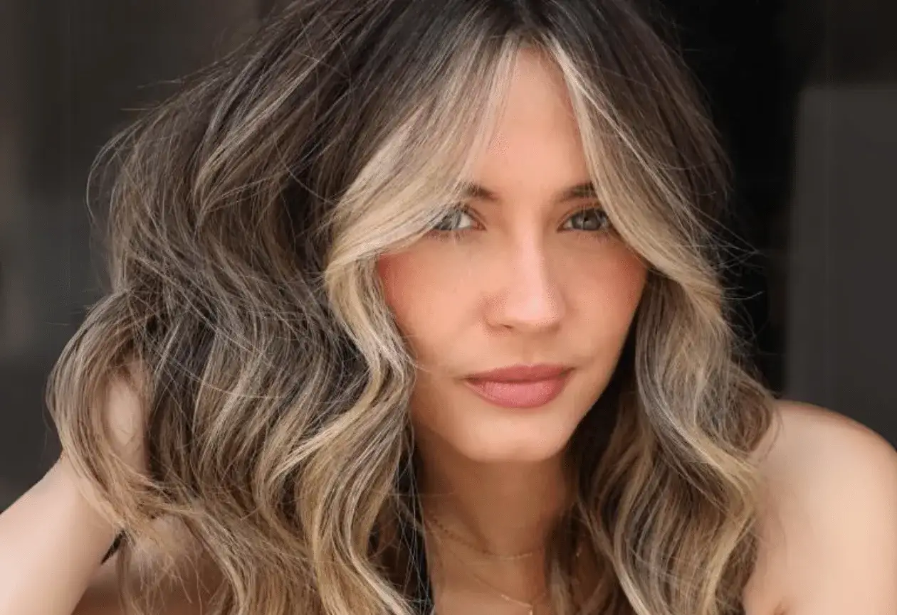 Frauenporträt mit welligem Haar und face framing highlights blonde Strähnen, die das Gesicht umspielen.