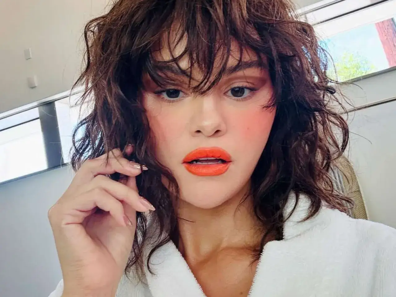 Selena Gomez mit einem lässigen Wolf Cut kurz, leuchtend orange Lippen und viel Rouge.