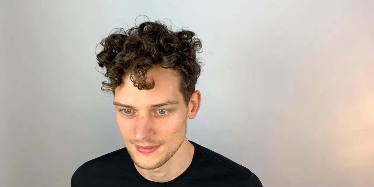 Junger Mann mit vollen, dunklen Locken. Ein Beispiel, wie man locken jungs stylen kann.