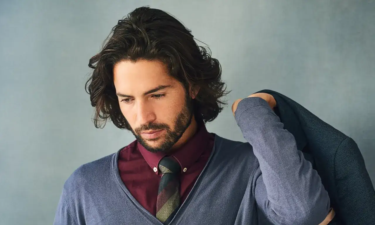 Mann mit langen Haaren und Bart, trägt Hemd, Krawatte und Pullover, legt Sakko über die Schulter. Sein bro flow ist beeindruckend.