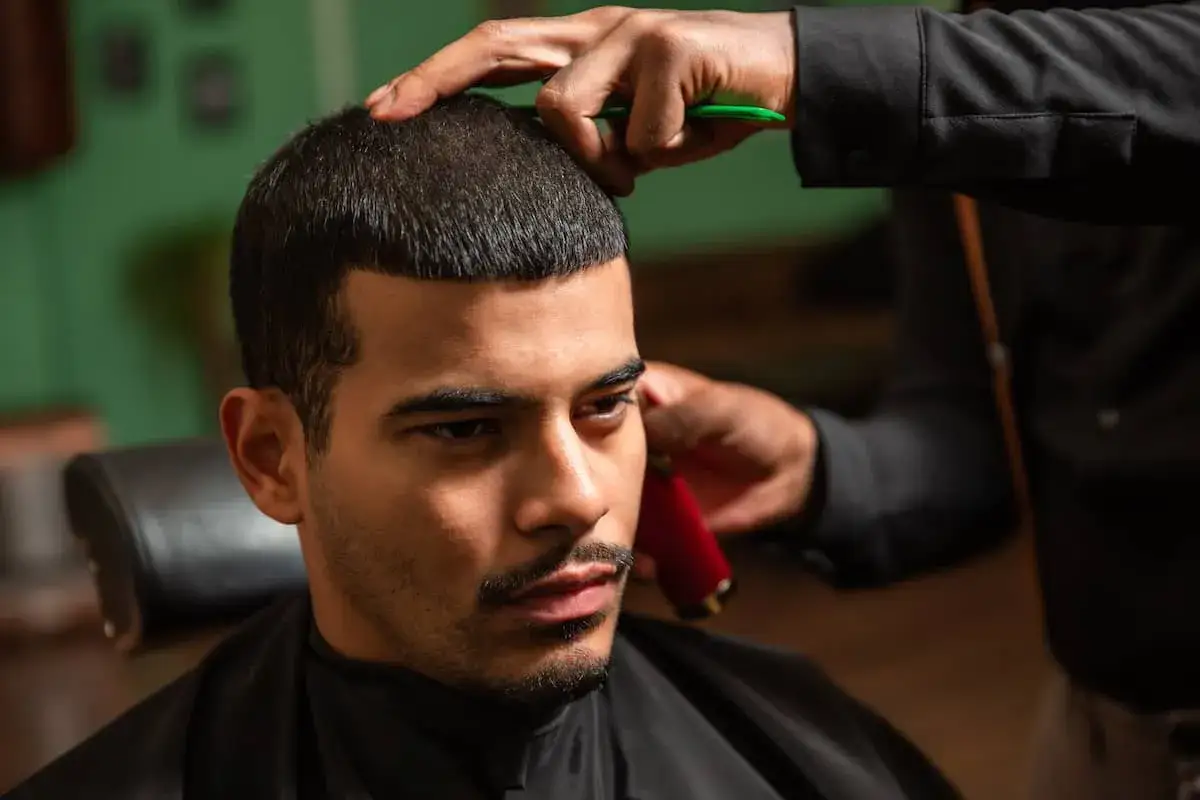 Mann mit Buzz Cut beim Friseur. Hände des Friseurs mit Schere und Trimmer.