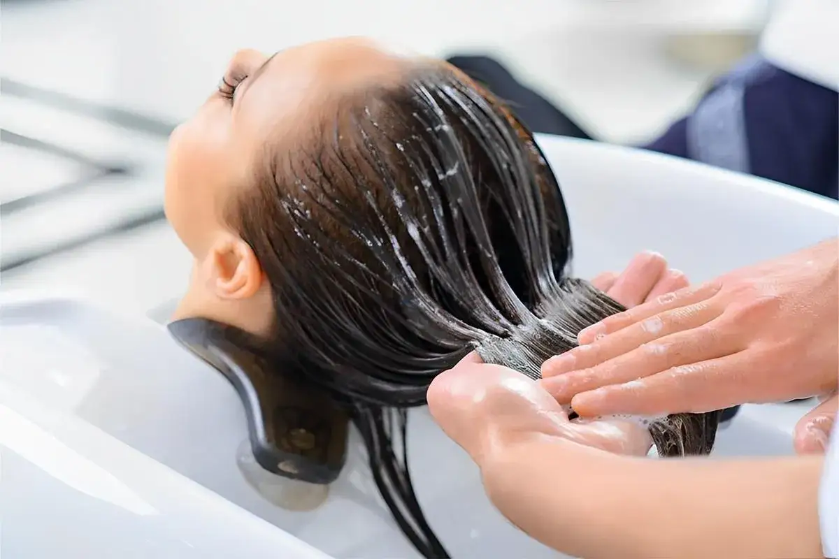 Eine Person erhält eine Haarwäsche mit Conditioner. Der Conditioner macht das Haar weich und glänzend.
