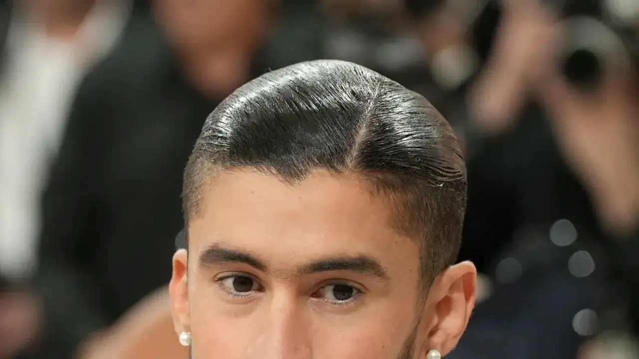 Ein Mann mit glänzendem, zur Seite gescheiteltem Haar, einem modernen fasson haarschnitt und einem Perlenohrring.