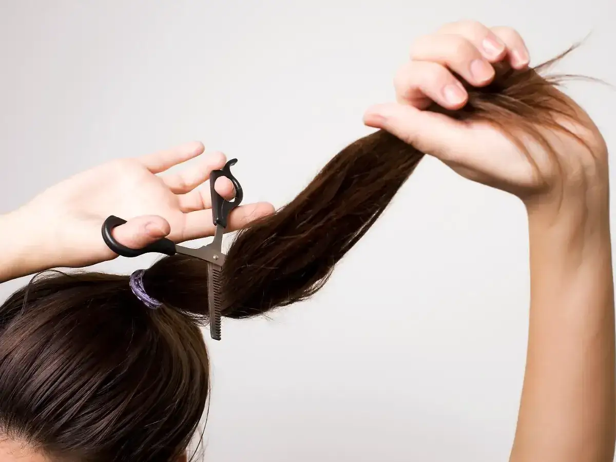 Frau schneidet sich mit einer Effilierschere die Haare, um einen Stufenschnitt selber zu schneiden.