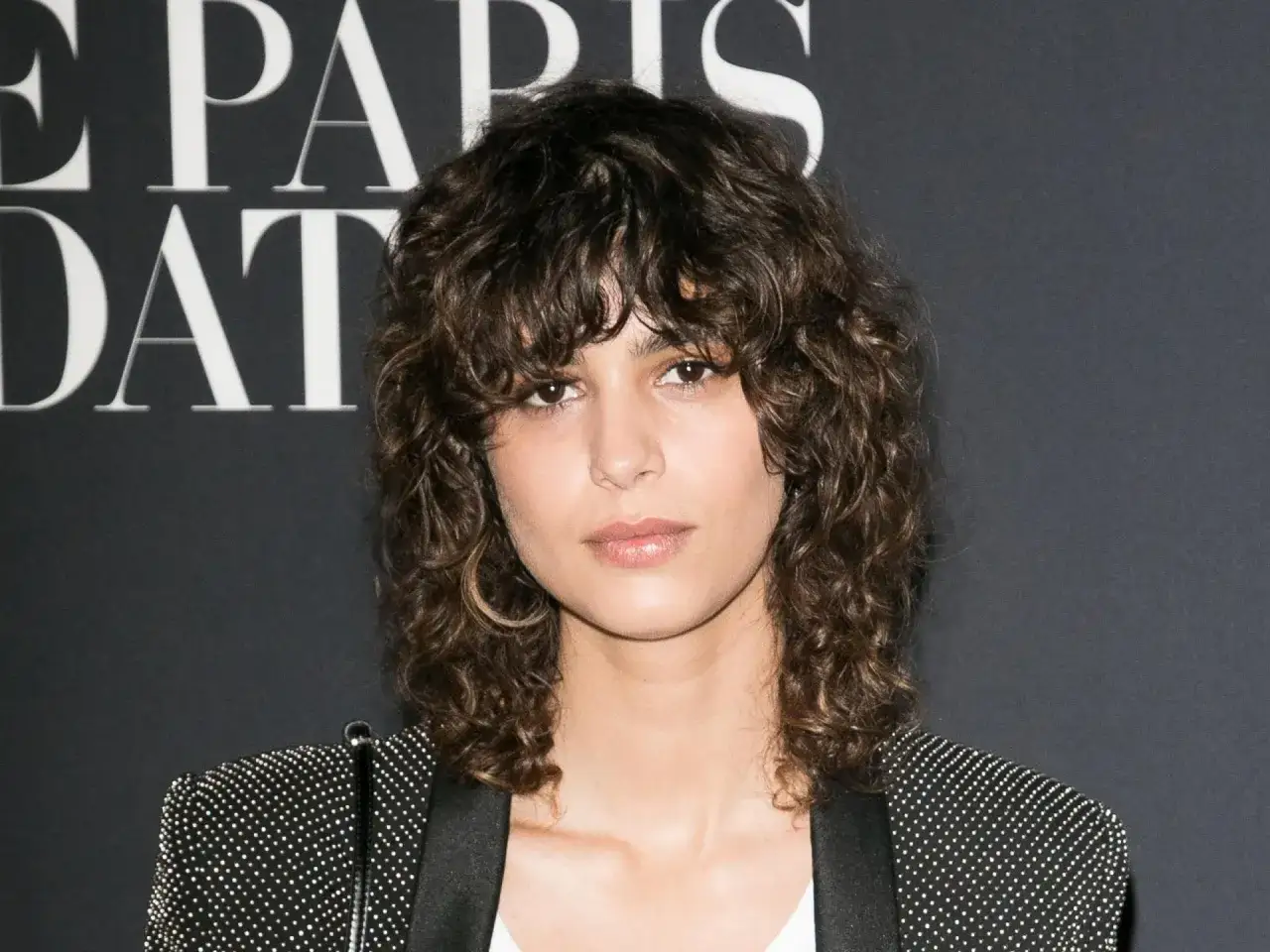 Frau mit kurzen Haaren Locken und einem funkelnden Blazer.