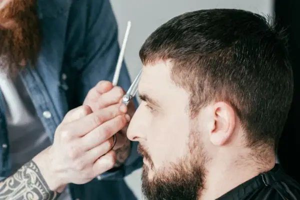 Ein Mann bekommt einen Caesar Cut. Der Friseur schneidet ihm mit einer Schere die Haare.
