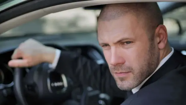 Mann mit Buzz Cut Mid Fade im Anzug fährt Auto.